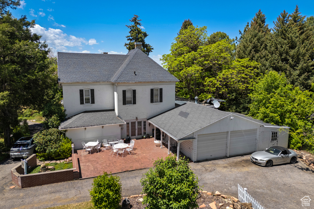 View of front facade featuring roof with shingles, a chimney, driveway, stucco siding, and a garage
