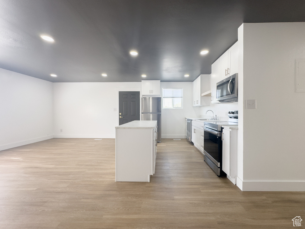 Kitchen with stainless steel appliances, a kitchen island, light wood-style floors, white cabinetry, and recessed lighting