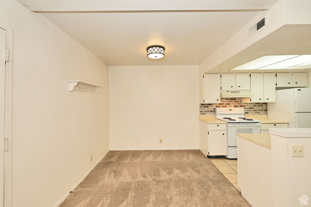 Kitchen with white appliances, under cabinet range hood, light countertops, decorative backsplash, and light carpet
