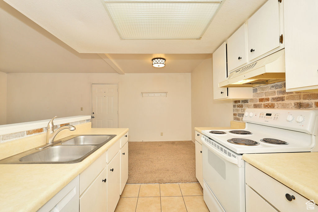Kitchen featuring white electric stove, light carpet, under cabinet range hood, light countertops, and white cabinets