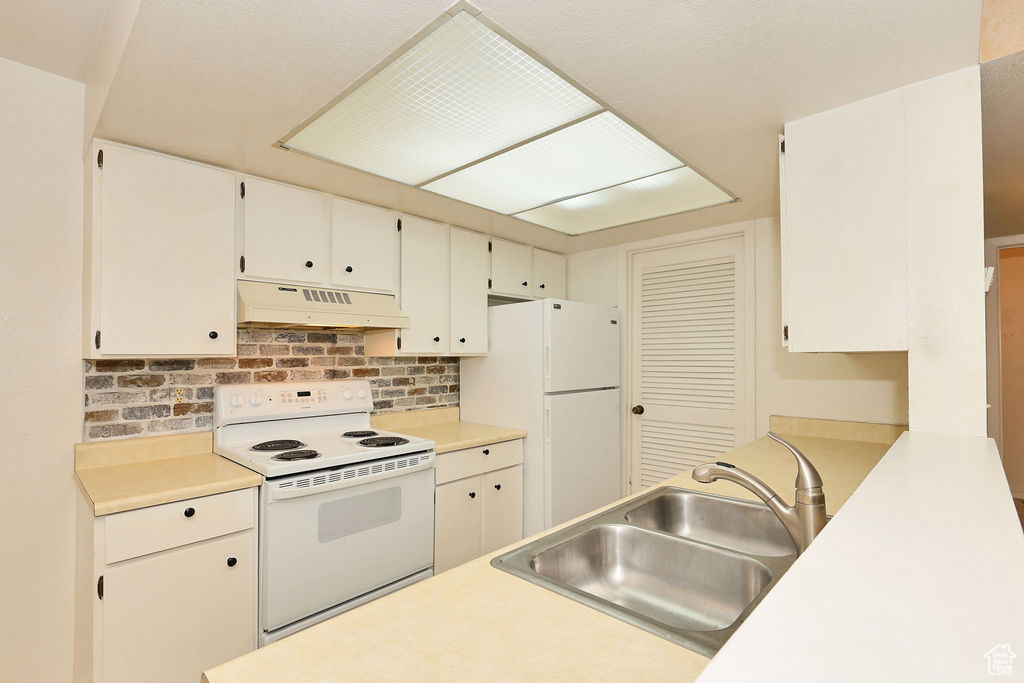 Kitchen featuring white appliances, ventilation hood, backsplash, light countertops, and white cabinets