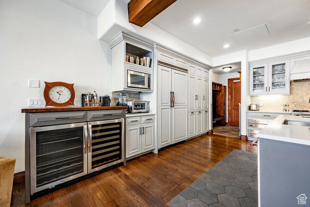 Kitchen with built in appliances, dark wood-style flooring, tasteful backsplash, glass insert cabinets, and light countertops