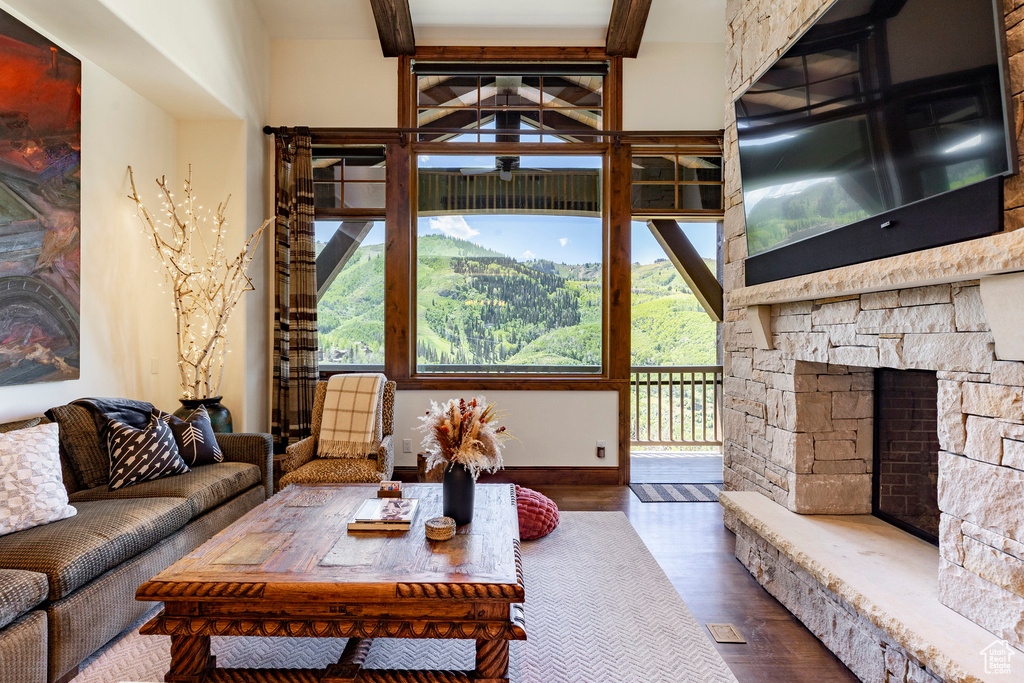 Living area with plenty of natural light, a fireplace, wood finished floors, beamed ceiling, and ceiling fan