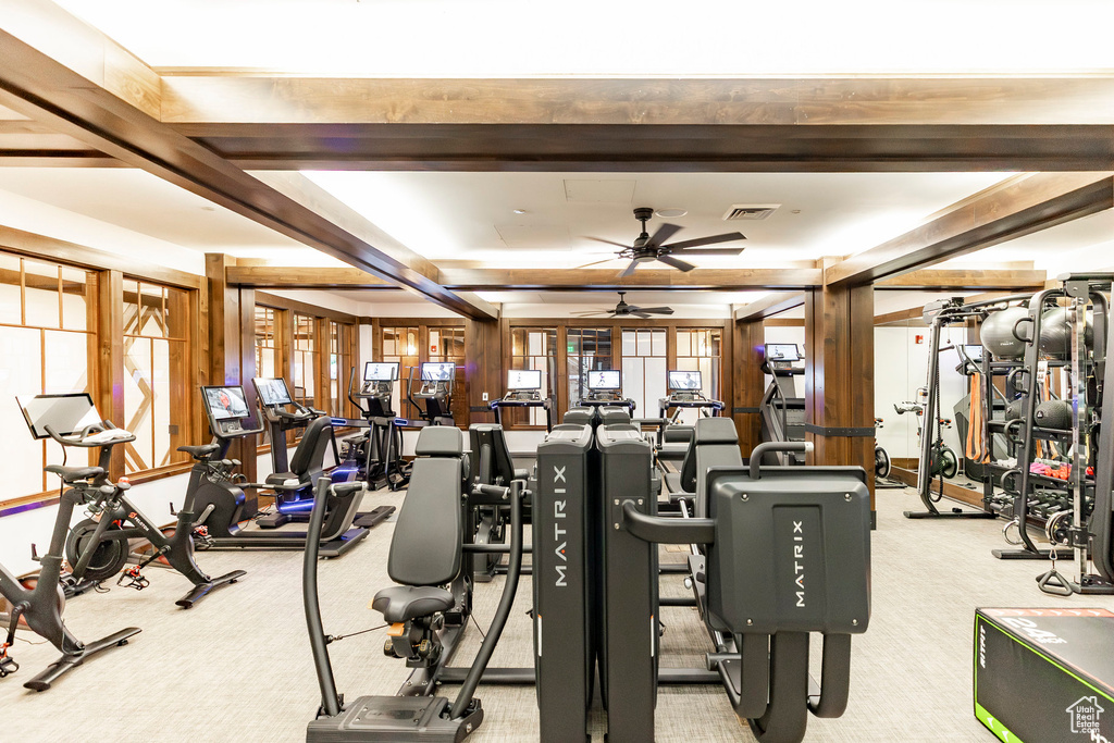 Exercise room featuring a ceiling fan, carpet floors, and beam ceiling