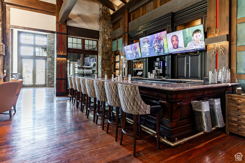 Indoor dry bar with wood-type flooring, high vaulted ceiling, and beamed ceiling