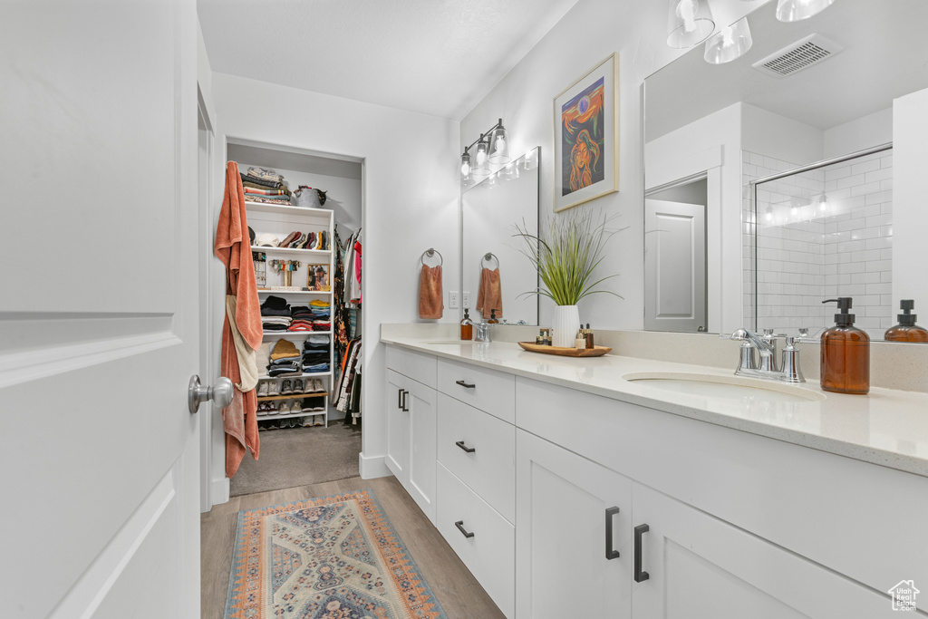 Bathroom featuring double vanity, a stall shower, wood finished floors, and a walk in closet