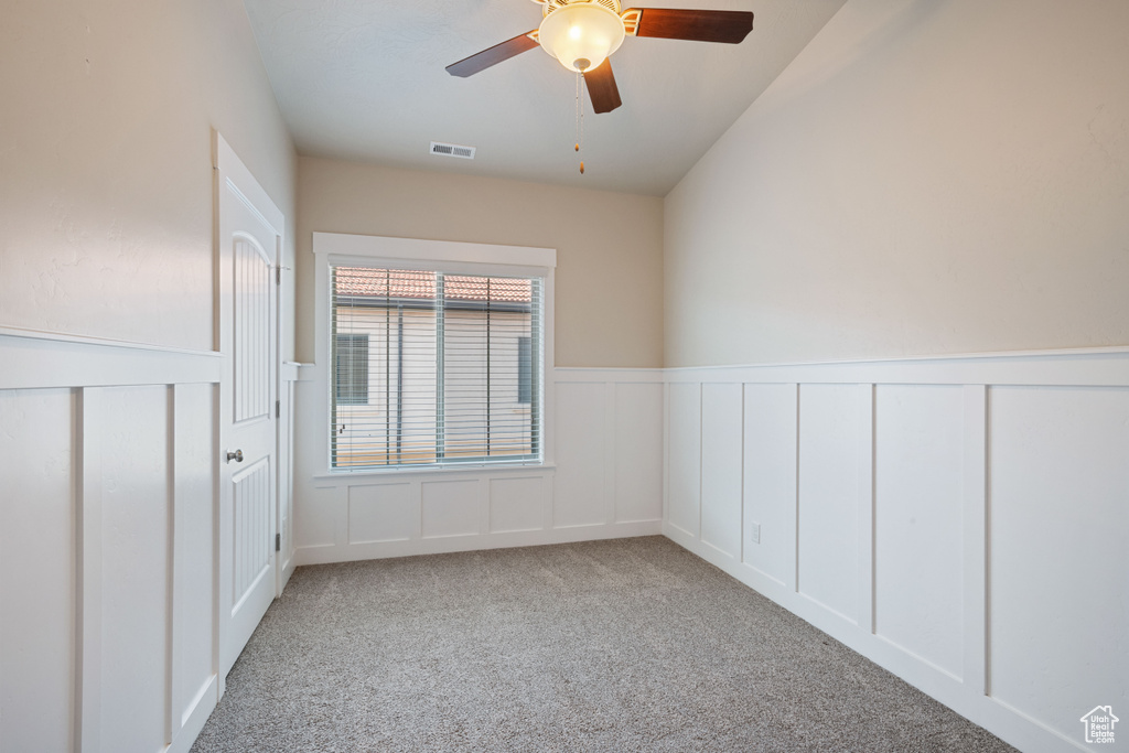 Carpeted spare room featuring a decorative wall, a ceiling fan, and a wainscoted wall