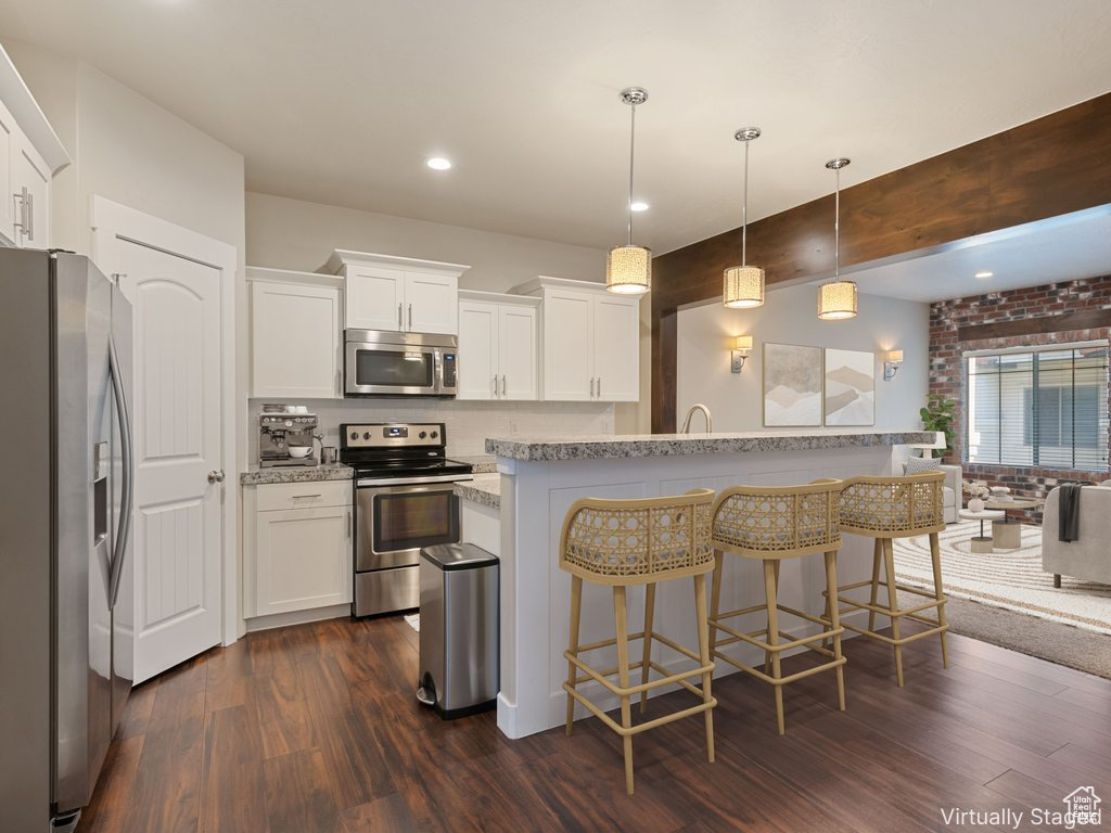 Kitchen with stainless steel appliances, dark wood-type flooring, a breakfast bar, white cabinets, and recessed lighting