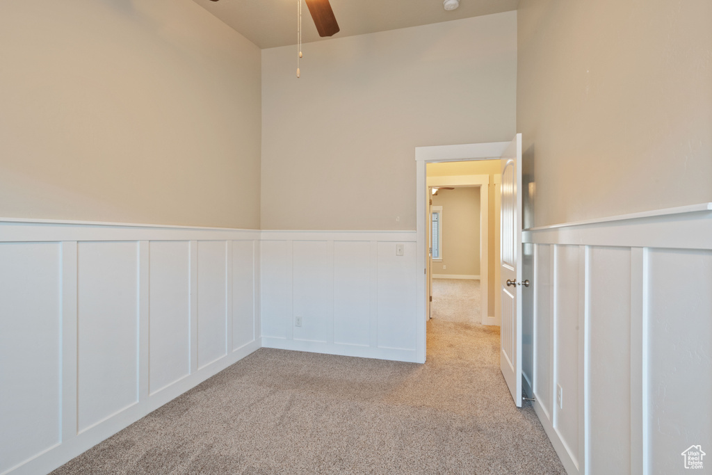 Carpeted spare room with ceiling fan, a decorative wall, and wainscoting