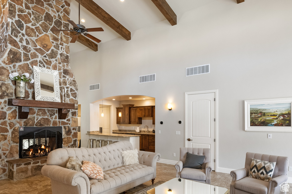Living area featuring a high ceiling, a ceiling fan, a stone fireplace, beamed ceiling, and arched walkways