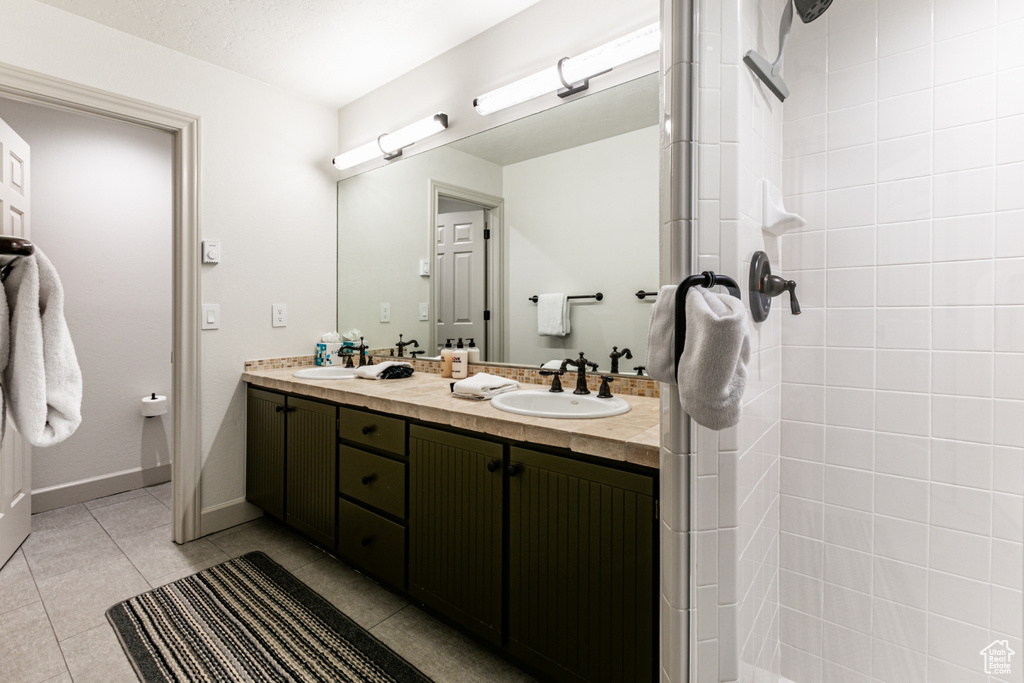 Full bath with double vanity, tile patterned flooring, and a tile shower