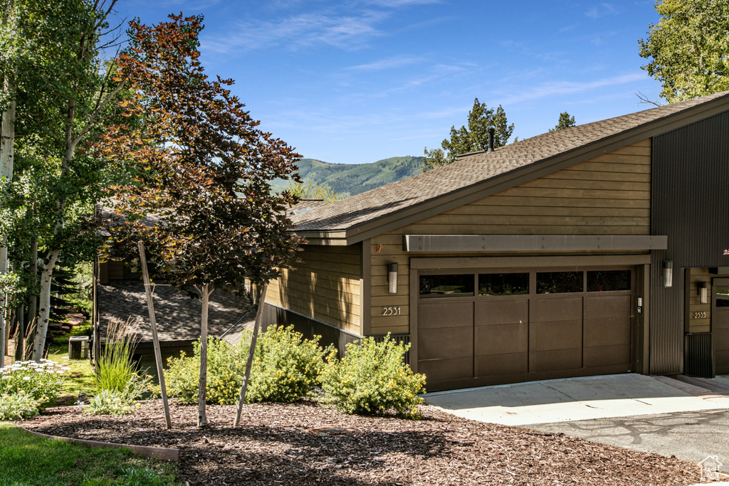 View of side of property featuring a mountain view, a garage, and roof with shingles