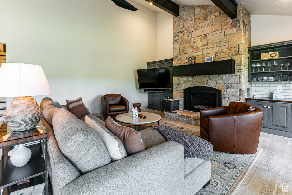 Living area with light wood finished floors, beamed ceiling, and a stone fireplace