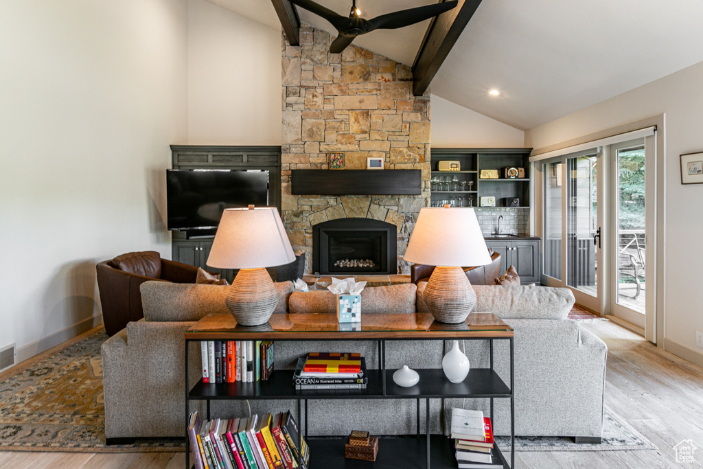 Living room with wood finished floors, ceiling fan, and a stone fireplace