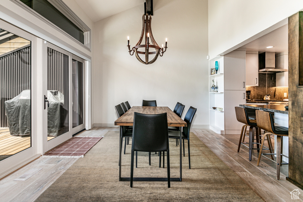Dining area featuring light wood-type flooring, a chandelier, and a high ceiling
