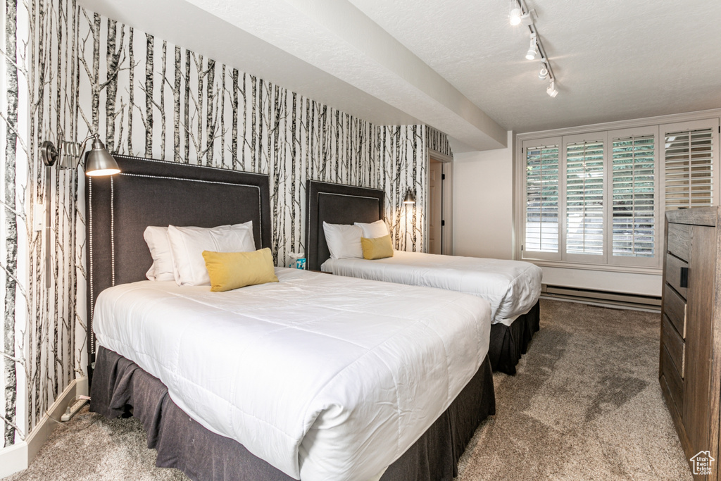 Carpeted bedroom featuring wallpapered walls, rail lighting, and baseboard heating