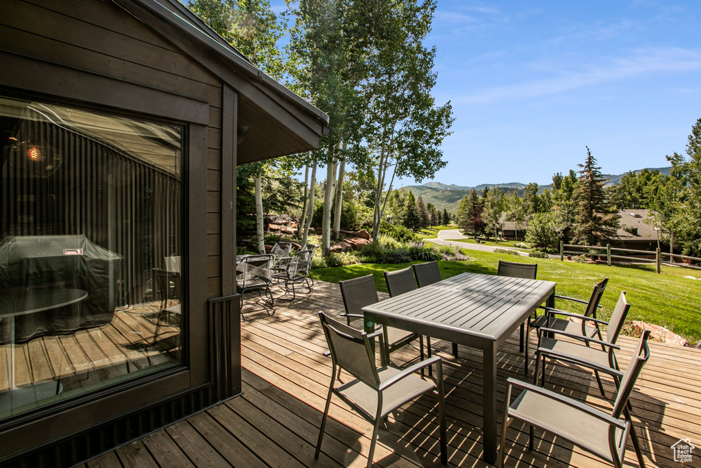 Deck with outdoor dining space, a mountain view, a lawn, and a grill