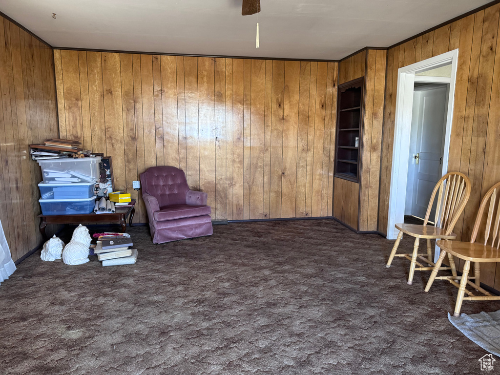 Living area with wood walls, carpet flooring, a ceiling fan, and built in features