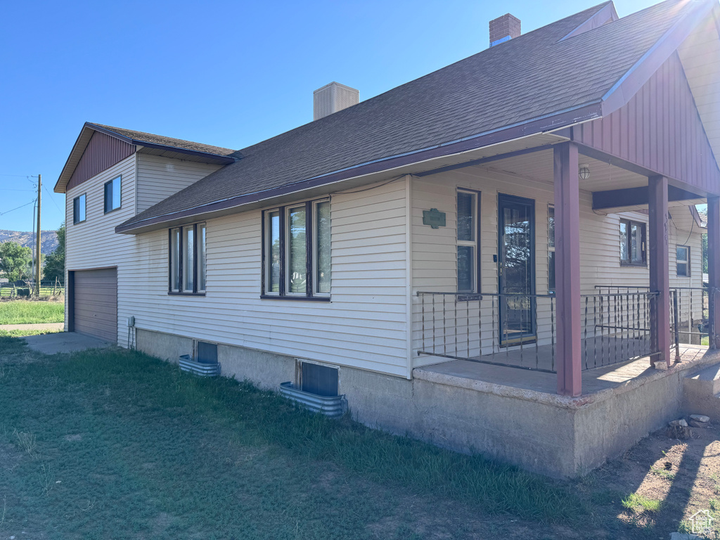 View of side of property with covered porch, a chimney, an attached garage, and roof with shingles