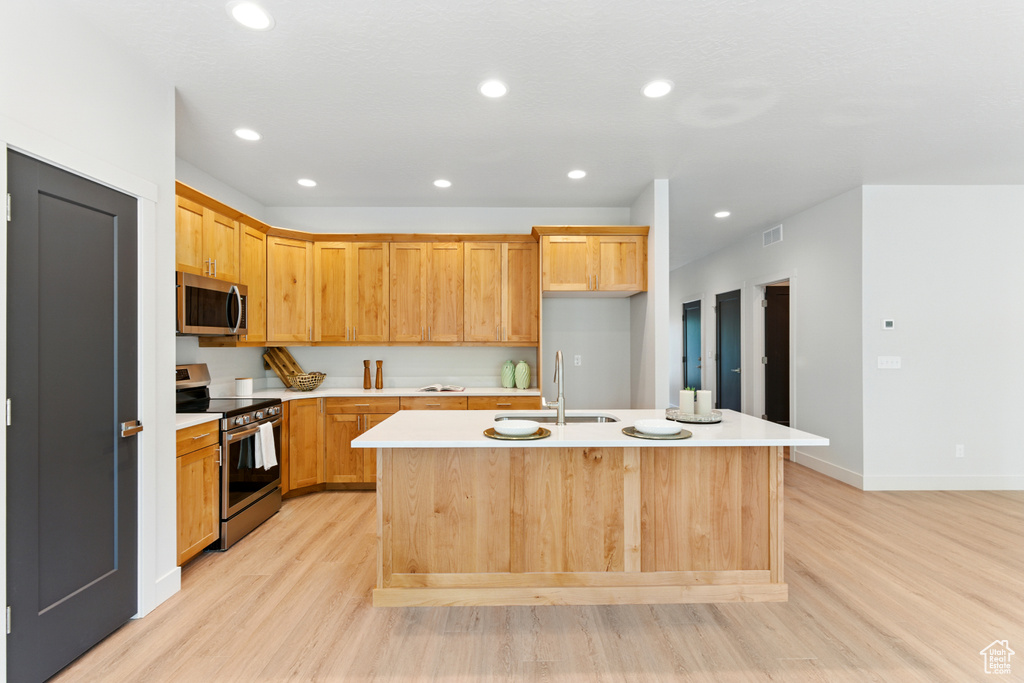 Kitchen featuring stainless steel appliances, light wood-style floors, light countertops, a center island with sink, and recessed lighting