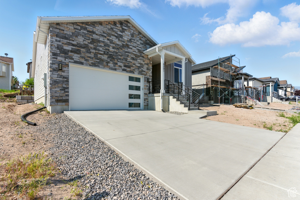 Modern home with a residential view, concrete driveway, stone siding, and an attached garage