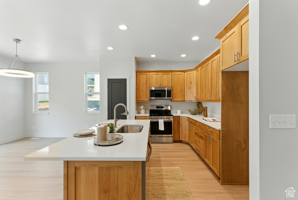 Kitchen with stainless steel appliances, a kitchen island with sink, light countertops, light wood-style flooring, and recessed lighting