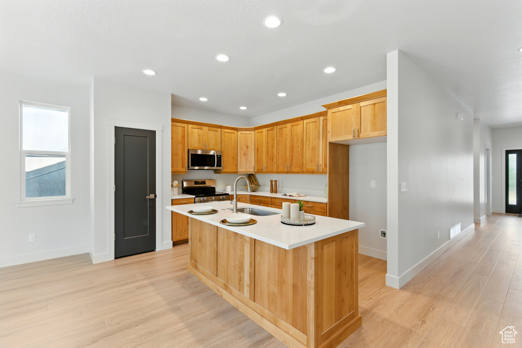 Kitchen with appliances with stainless steel finishes, light wood-style flooring, light countertops, a center island with sink, and recessed lighting