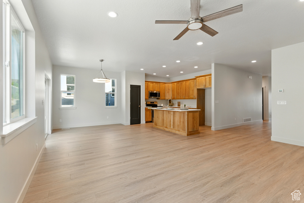 Kitchen featuring stainless steel microwave, open floor plan, recessed lighting, light countertops, and a ceiling fan