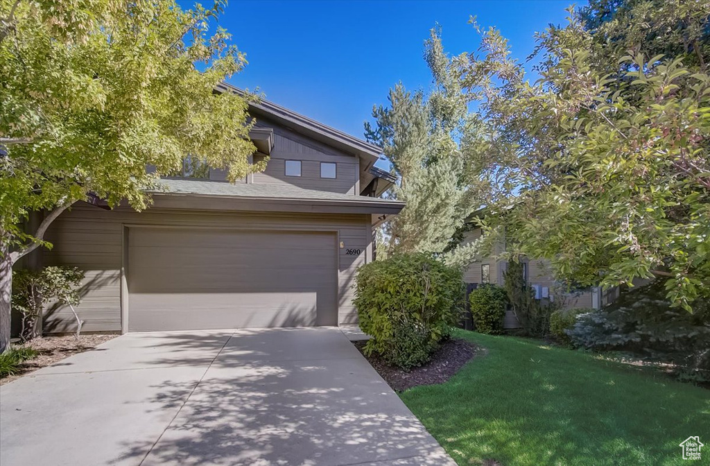 View of front of property with concrete driveway, an attached garage, and a front lawn