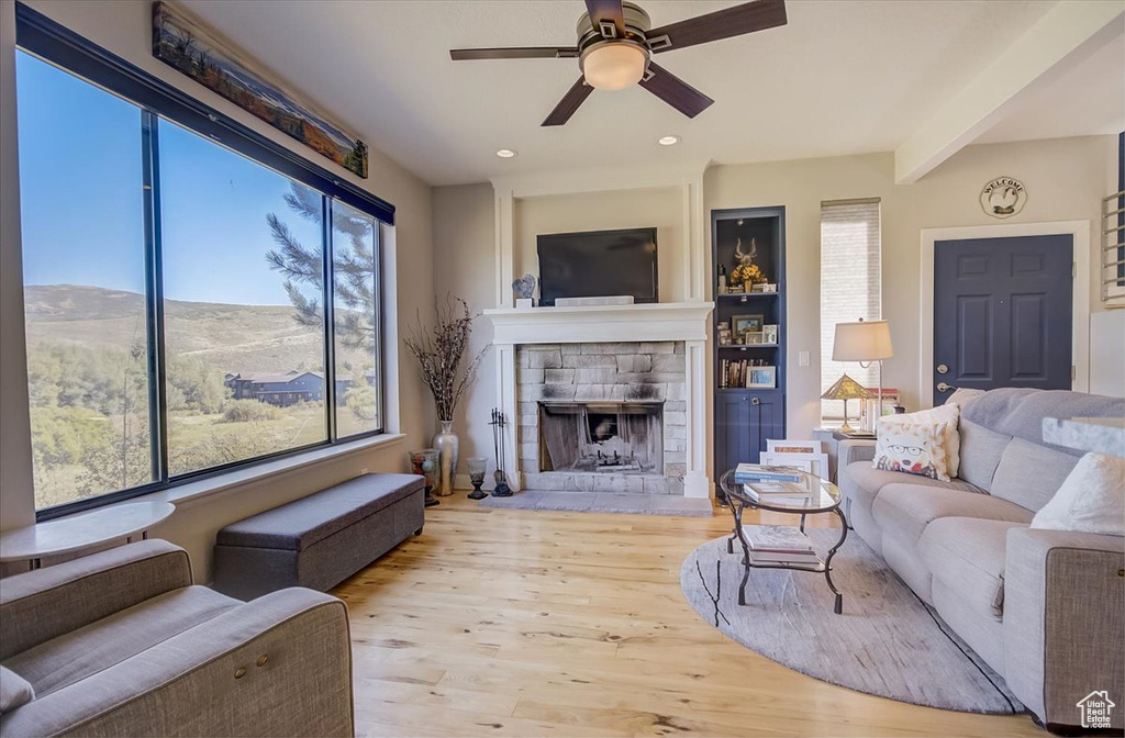 Living room with wood finished floors, ceiling fan, a stone fireplace, and recessed lighting