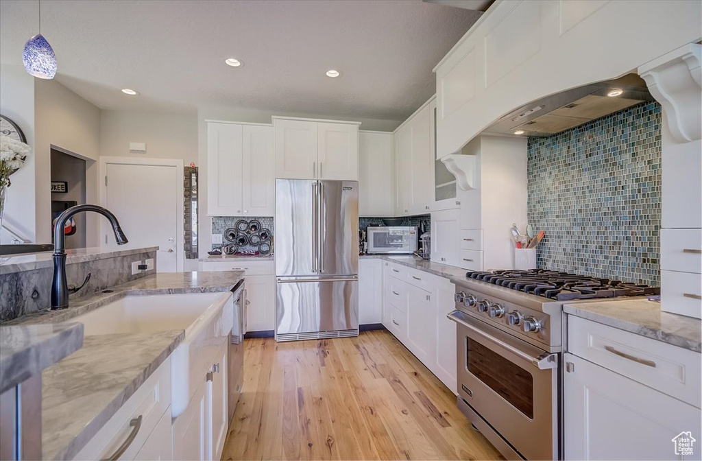Kitchen with high quality appliances, decorative backsplash, light stone counters, white cabinets, and light wood finished floors