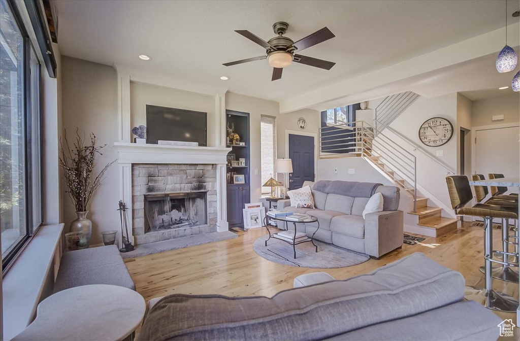 Living room featuring stairs, wood finished floors, a ceiling fan, a stone fireplace, and recessed lighting
