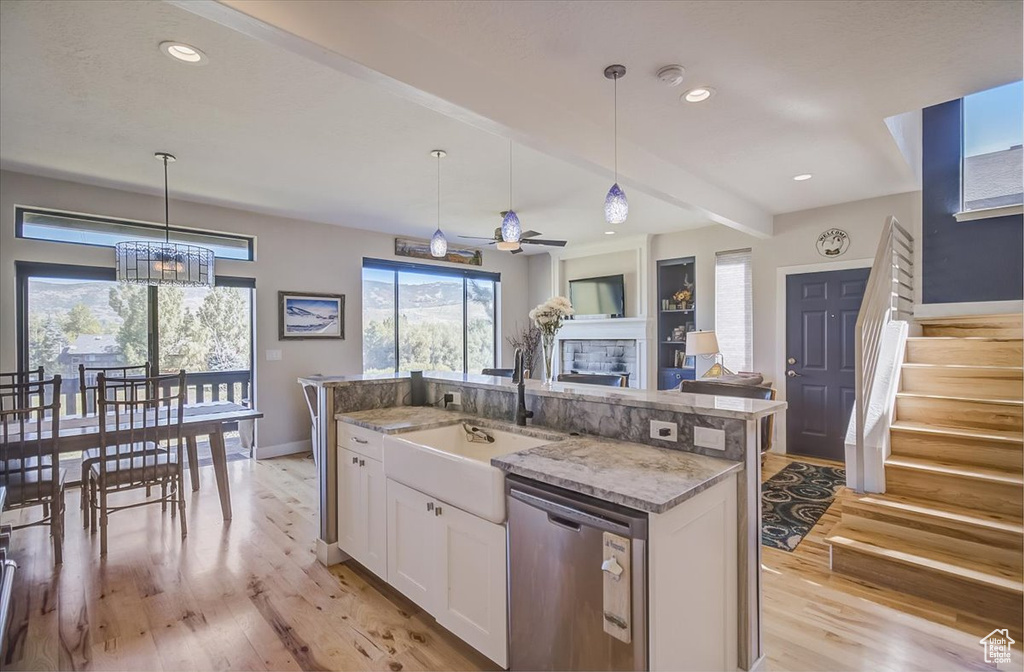 Kitchen featuring stainless steel dishwasher, light wood-type flooring, white cabinetry, decorative light fixtures, and a fireplace