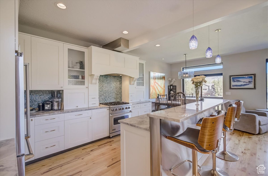 Kitchen with high end stove, light wood-style flooring, backsplash, white cabinetry, and light stone countertops
