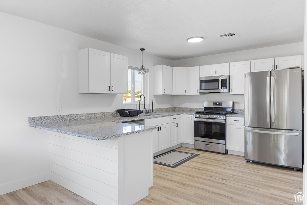 Kitchen with appliances with stainless steel finishes, a peninsula, light wood finished floors, white cabinets, and light stone countertops