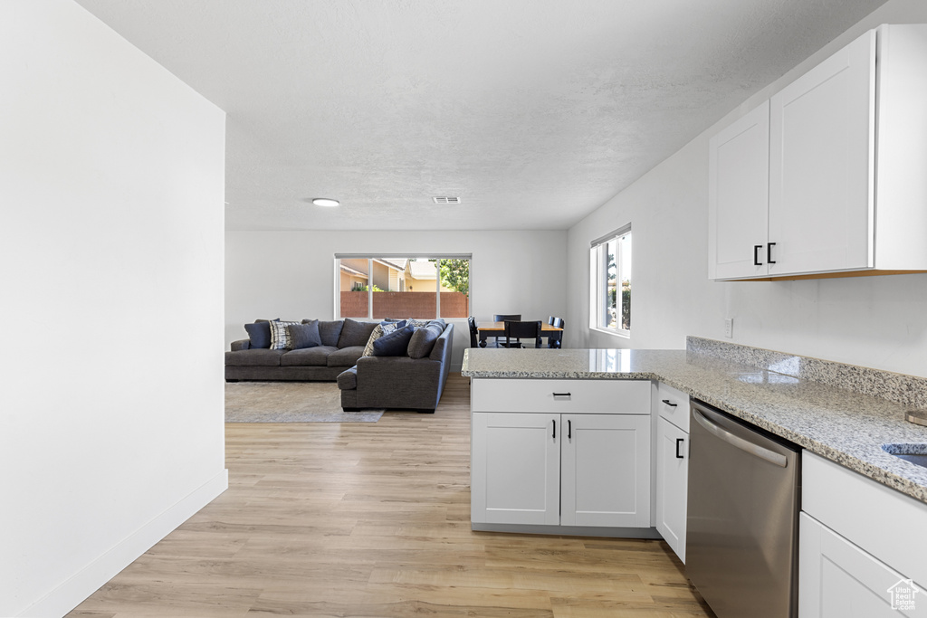 Kitchen with stainless steel dishwasher, white cabinetry, a peninsula, and light stone counters