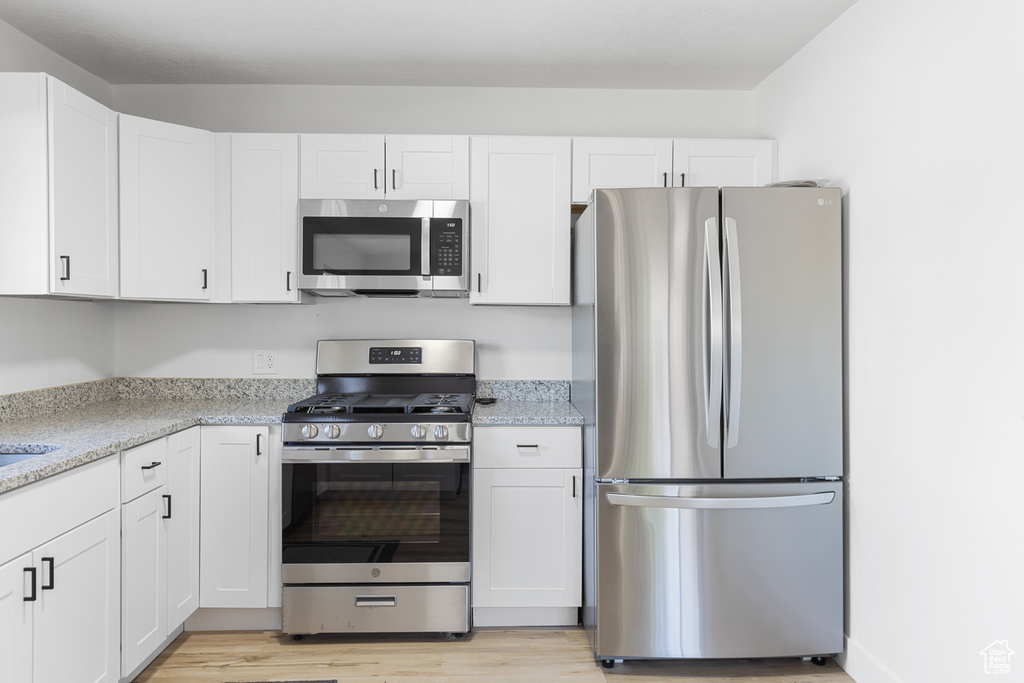 Kitchen featuring stainless steel appliances, light wood finished floors, white cabinets, and light stone counters