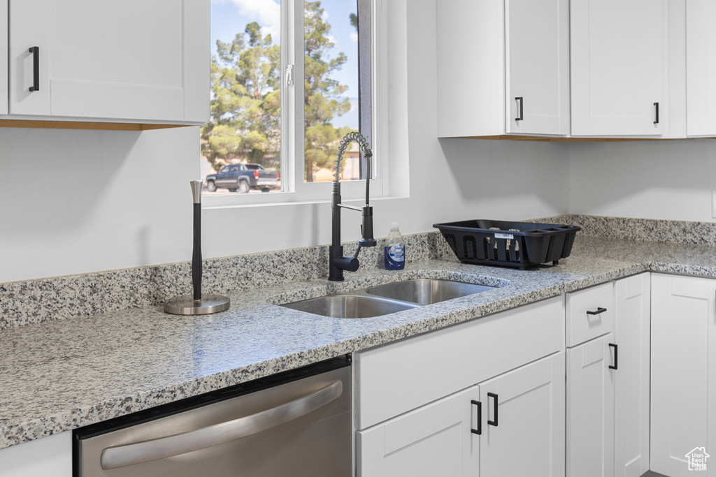 Kitchen featuring stainless steel dishwasher, white cabinetry, and light stone countertops