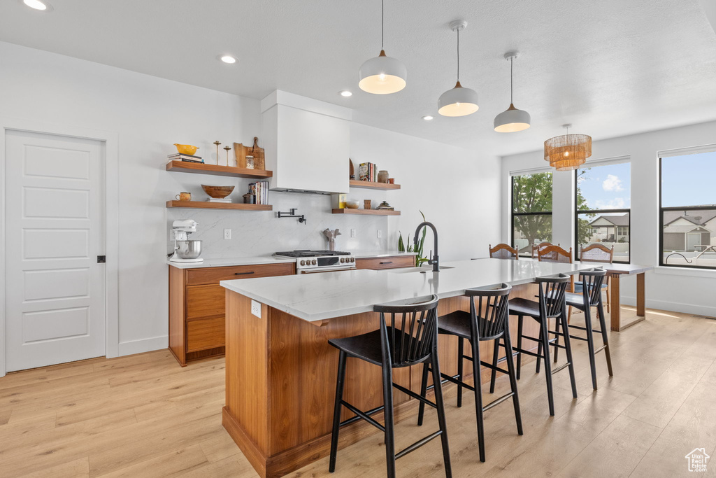 Kitchen featuring open shelves, range with gas stovetop, light wood finished floors, backsplash, and brown cabinetry