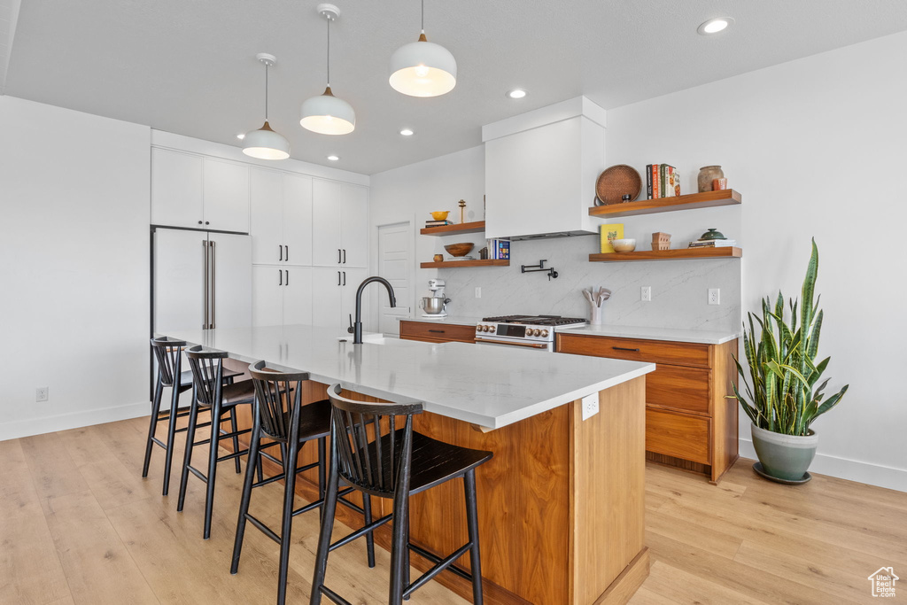 Kitchen featuring open shelves, premium appliances, light countertops, light wood-type flooring, and backsplash