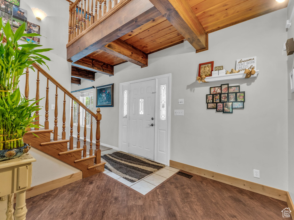 Entrance foyer with a wooden ceiling with exposed beams, wood finished floors, and stairs