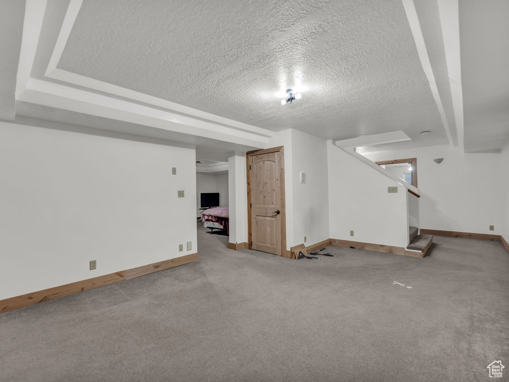 Finished below grade area with a textured ceiling, carpet floors, and stairway