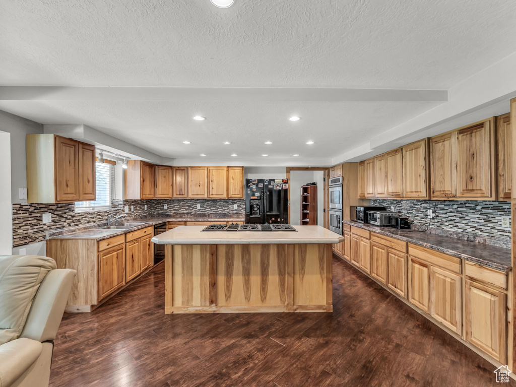 Kitchen with appliances with stainless steel finishes, decorative backsplash, a kitchen island, dark wood-type flooring, and recessed lighting