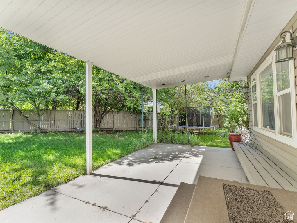 Fenced backyard featuring a trampoline and a patio area
