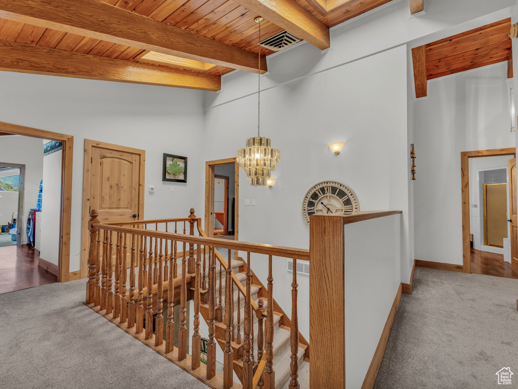Hall featuring an upstairs landing, carpet floors, a chandelier, a wood ceiling with exposed beams, and a towering ceiling