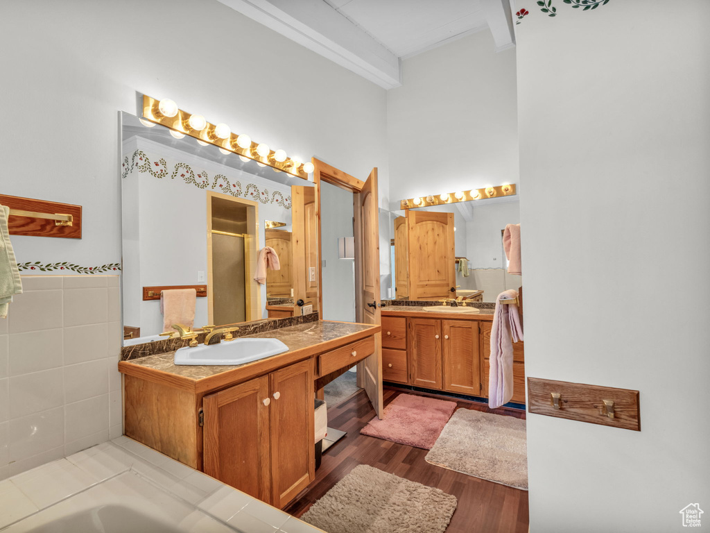 Full bathroom with a stall shower, two vanities, a high ceiling, wood finished floors, and a bathtub