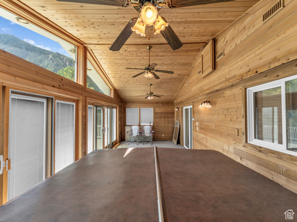 Unfurnished sunroom with lofted ceiling, ceiling fan, wooden walls, wood ceiling, and a mountain view