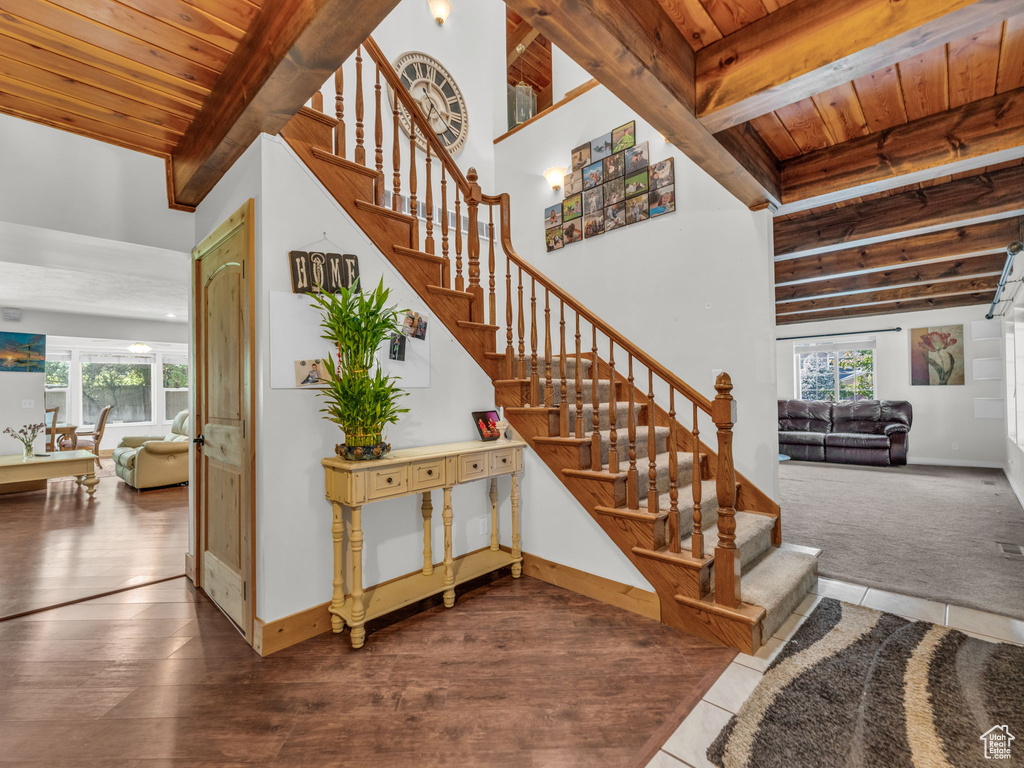 Stairs featuring a wooden ceiling with exposed beams, healthy amount of natural light, and wood finished floors