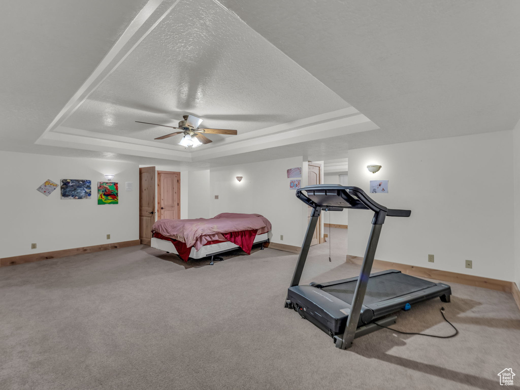 Carpeted bedroom featuring a raised ceiling, a ceiling fan, and a textured ceiling