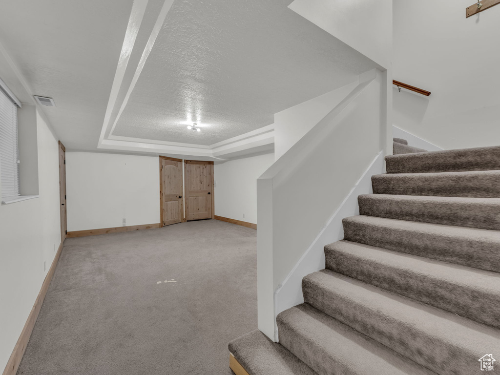 Finished below grade area featuring stairway, light carpet, and a textured ceiling